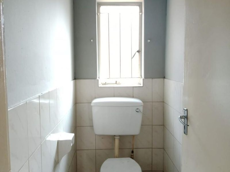 A compact, functional guest toilet featuring tiled walls and flooring, a standard white toilet suite, and a window with security bars.