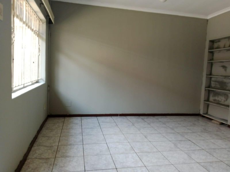 An empty bedroom featuring tiled flooring, a window with security bars, and built-in shelving units.