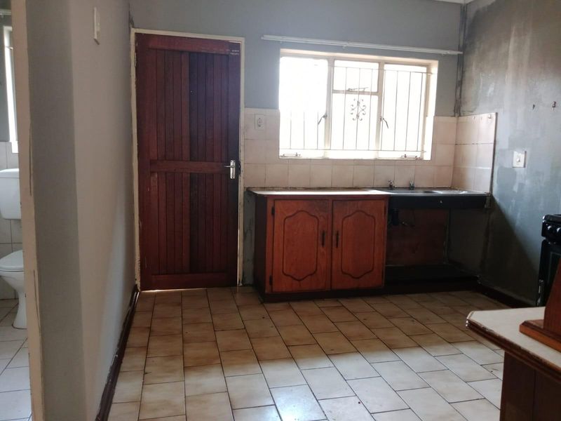 A dated kitchen area featuring basic cabinetry, a sink, and tiled flooring, requiring renovation and finishing to improve functionality and aesthetic appeal.