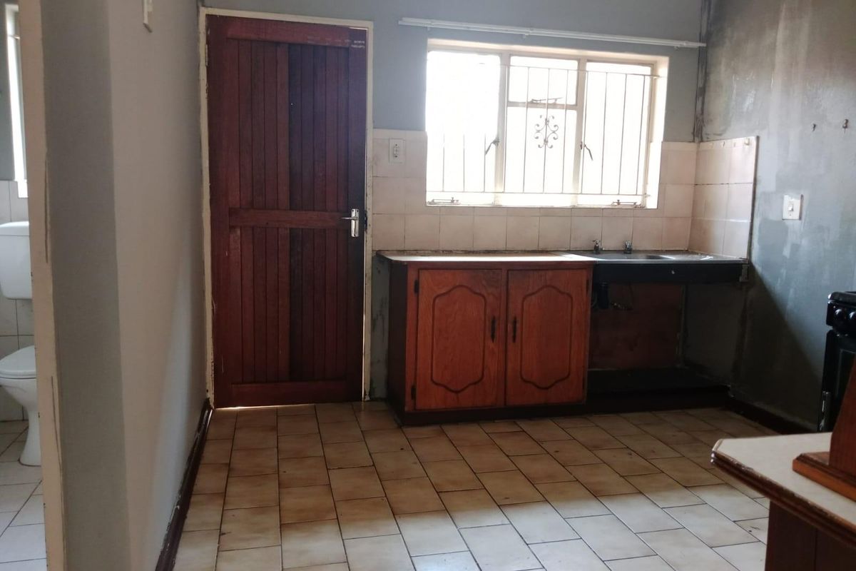 A dated kitchen area featuring basic cabinetry, a sink, and tiled flooring, requiring renovation and finishing to improve functionality and aesthetic appeal.