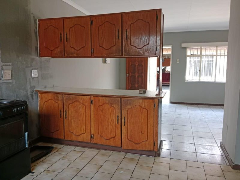 A dated kitchen area featuring wooden cabinetry, tiled flooring, and an unfinished wall section, offering potential for renovation and modernization.