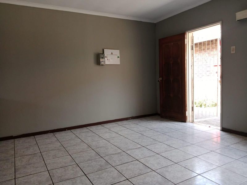 An empty living area featuring neutral tiled flooring, a timber entrance door, and a wall-mounted electrical distribution board.