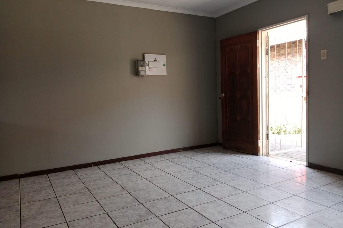 An empty living area featuring neutral tiled flooring, a timber entrance door, and a wall-mounted electrical distribution board.