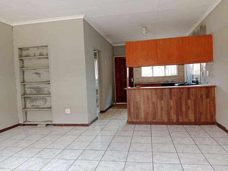 Open plan living and kitchen area featuring tiled flooring, a breakfast bar, and built-in shelving, offering a blank canvas for renovation.