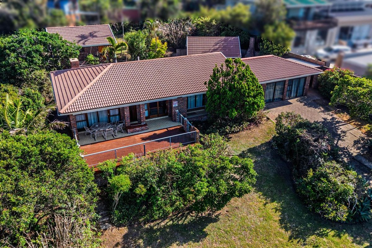Aerial view of a single-story brick house featuring a tiled roof, a spacious wooden deck, and a well-established garden with a paved driveway.