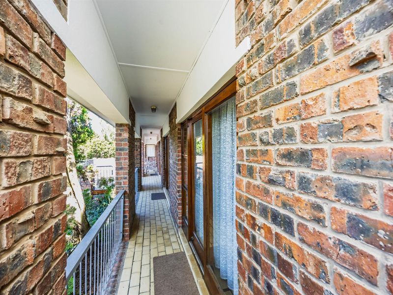 A covered outdoor balcony featuring exposed brick walls, tiled flooring, and a metal balustrade, providing access to the interior through sliding glass doors.