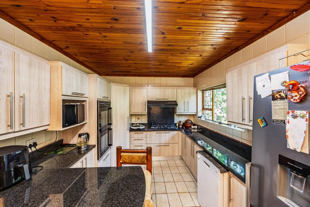 A functional kitchen featuring light wood cabinetry, dark granite countertops, a double wall oven, gas hob, and a distinctive timber-paneled ceiling.