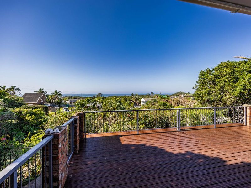Spacious elevated timber deck featuring brick pillars and metal balustrades, offering expansive views of the surrounding landscape and distant ocean.