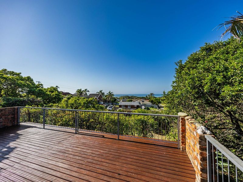 An elevated timber deck balcony featuring brick and metal balustrades, offering expansive views of the surrounding neighborhood and distant ocean.