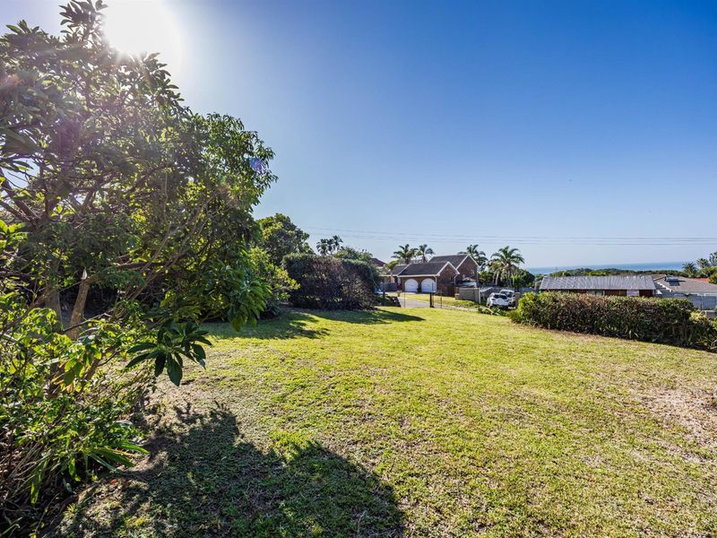 A spacious, sunlit garden area featuring established trees and hedging, offering a clear view towards the neighboring properties and distant horizon.