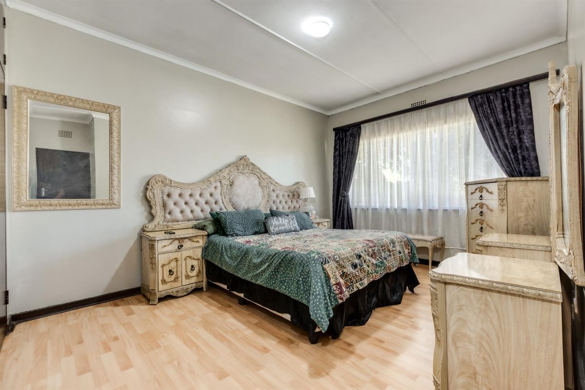 A well-maintained bedroom featuring light wood-look flooring, neutral wall finishes, and a large window with curtain tracks.