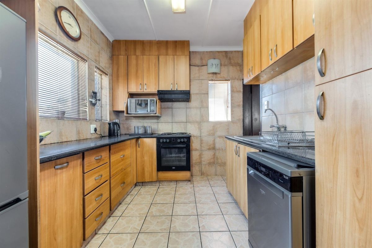 A functional kitchen featuring wood-finish cabinetry, granite-look countertops, tiled walls and flooring, and a built-in oven with extractor fan.