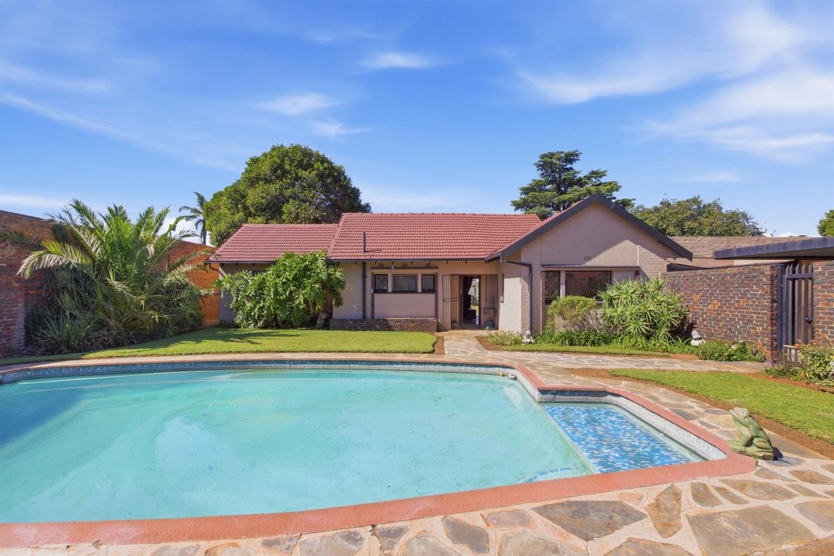 A rear view of the house featuring a swimming pool, paved patio area, and established garden with a tiled roof structure.