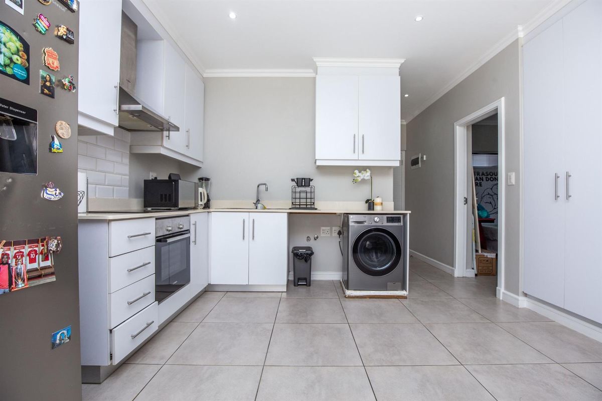 Modern kitchen featuring white cabinetry, subway tile backsplash, built-in oven, extractor fan, and tiled flooring with integrated laundry plumbing.