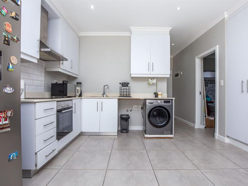 Modern kitchen featuring white cabinetry, subway tile backsplash, built-in oven, extractor fan, and tiled flooring with integrated laundry plumbing.
