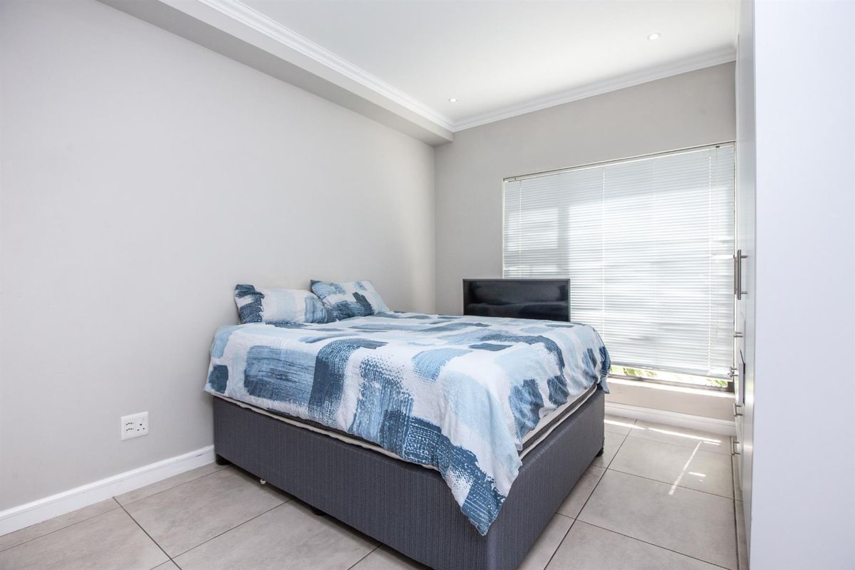 A well-maintained bedroom featuring neutral tiled flooring, built-in cupboards, recessed downlighting, and venetian blinds for privacy.