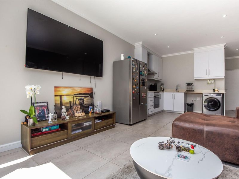 An open-plan living area featuring a modern kitchen with built-in cabinetry, tiled flooring, and recessed lighting, seamlessly integrated with the lounge space.