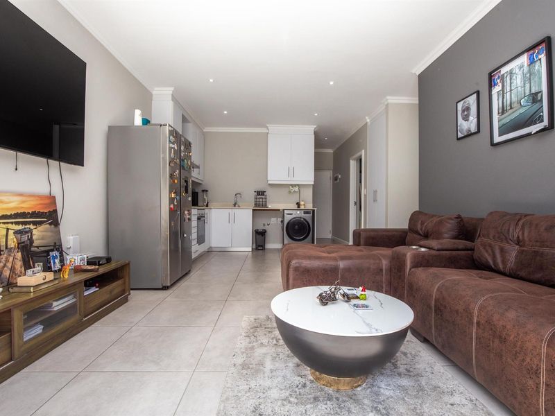 An open-plan living area featuring tiled flooring, recessed lighting, and a functional kitchen with built-in cabinetry and integrated appliances.