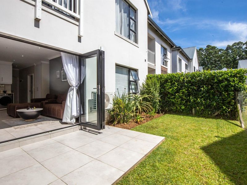 A well-maintained rear exterior view featuring a tiled patio, private garden with hedging, and bi-fold doors leading into the living area.