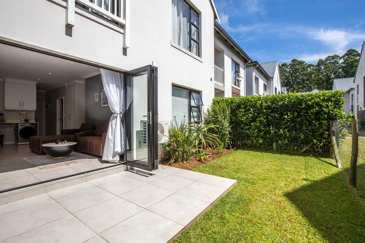 A well-maintained rear exterior view featuring a tiled patio, private garden with hedging, and bi-fold doors leading into the living area.