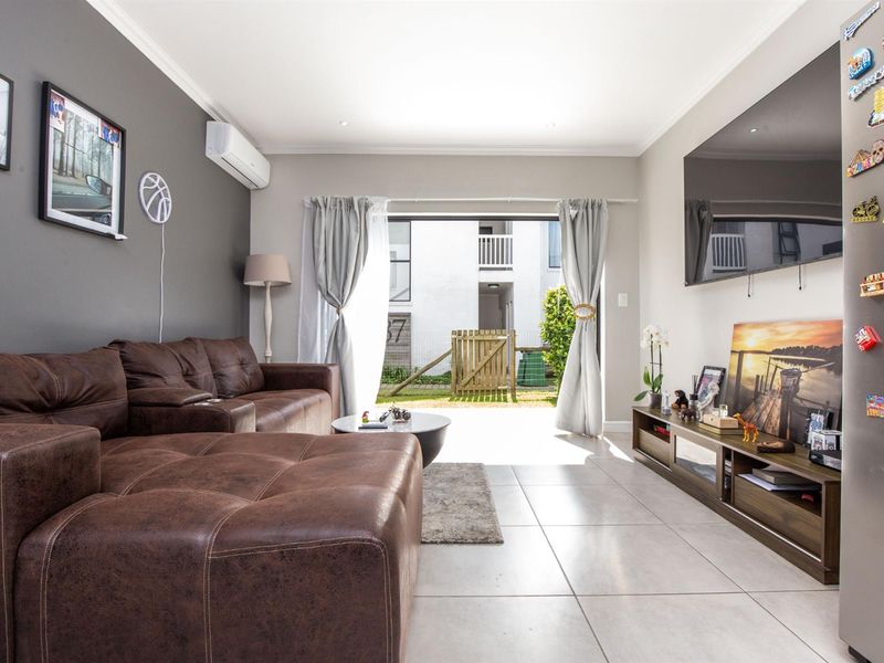 A well-maintained living room featuring tiled flooring, recessed lighting, and a split-system air conditioner, with direct access to an outdoor patio area.