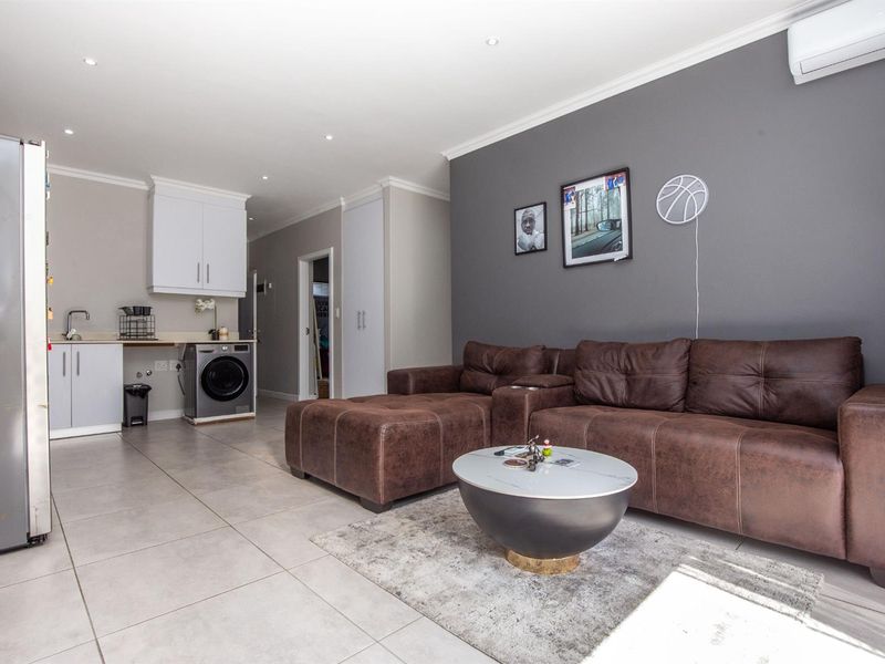 Open-plan living area featuring tiled flooring, recessed lighting, a compact kitchen prep area with built-in cabinetry, and a wall-mounted air conditioning unit.