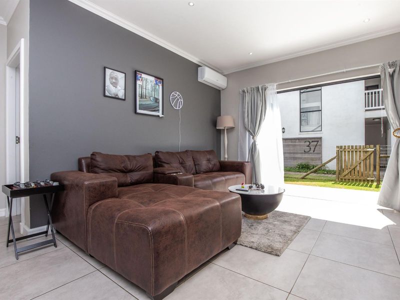 A well-maintained living room featuring tiled flooring, recessed lighting, and a split-system air conditioner, with direct access to an outdoor patio area.