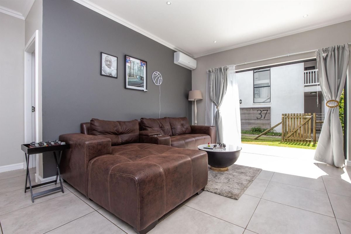 A well-maintained living room featuring tiled flooring, recessed lighting, and a split-system air conditioner, with direct access to an outdoor patio area.