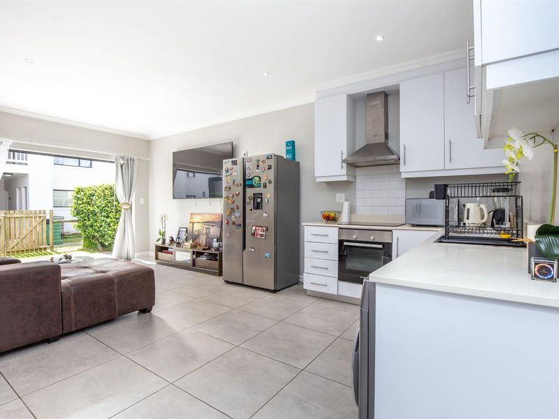 Modern open-plan living area featuring a well-appointed kitchen with built-in appliances, tiled flooring, and seamless access to an outdoor patio space.