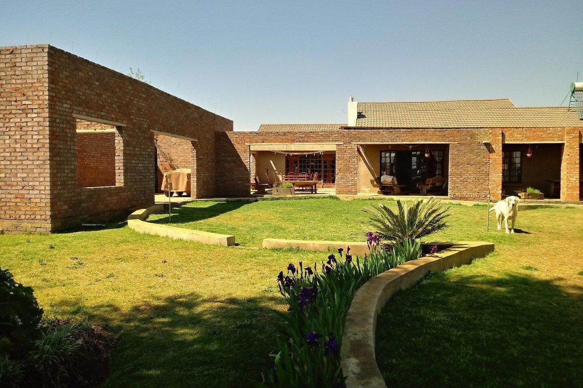 A spacious rear courtyard featuring exposed brick architecture, a manicured lawn, and a curved garden border, offering potential for further development or outdoor living.