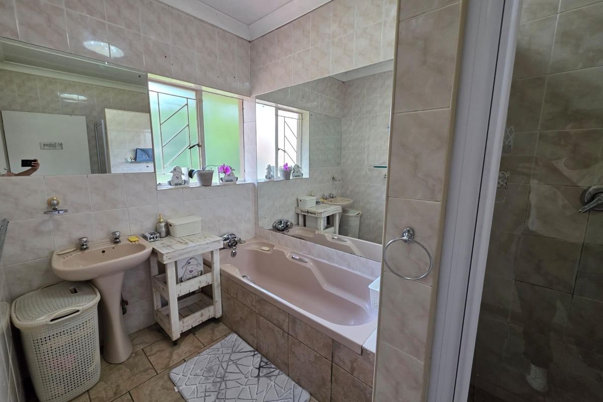 A dated bathroom featuring a built-in bathtub, pedestal sink, and wall-to-wall mirrors with neutral ceramic wall and floor tiling.
