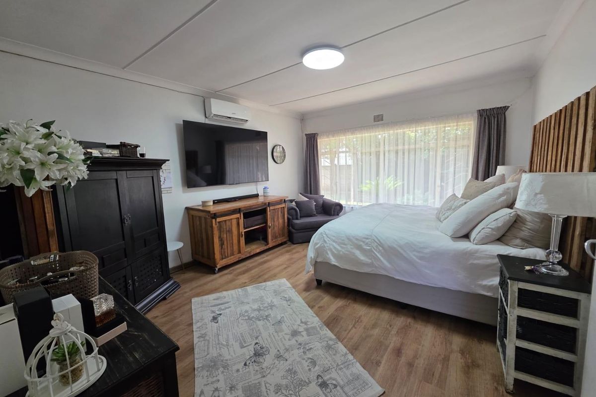 A spacious bedroom featuring wood-look flooring, a wall-mounted air conditioning unit, and large windows that provide ample natural light.