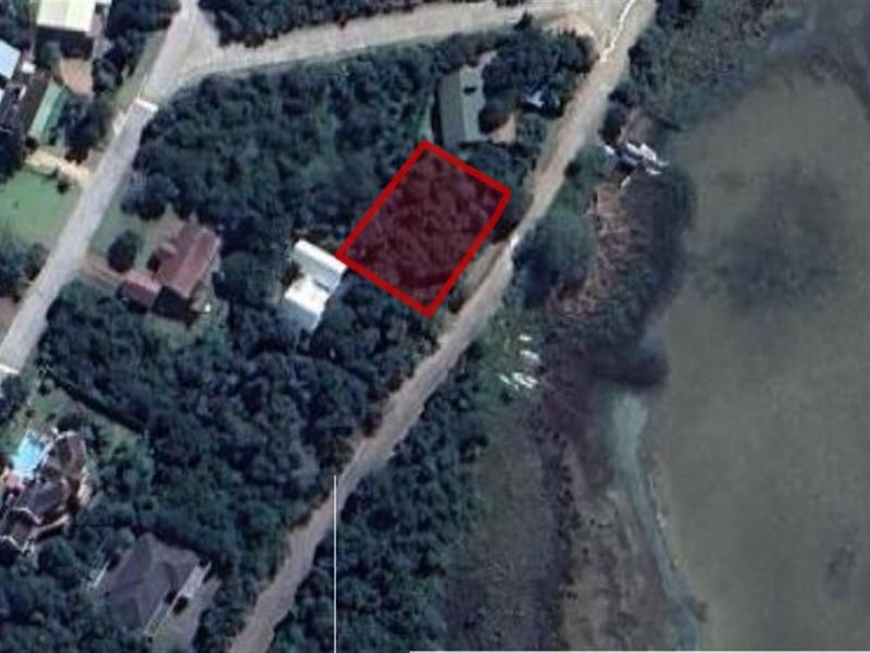 Aerial view of a vacant residential plot highlighted in red, situated in a coastal neighborhood near the water.