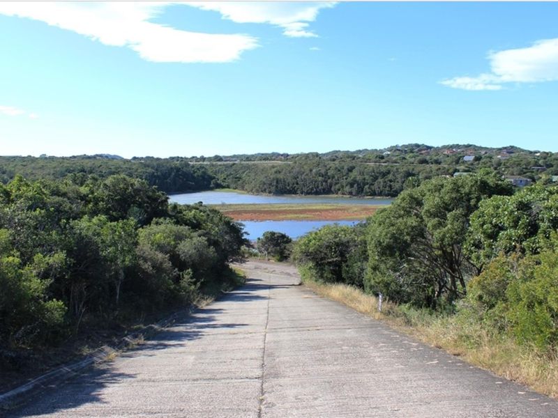 A view looking down a concrete driveway towards a scenic landscape featuring a lake and surrounding natural vegetation.