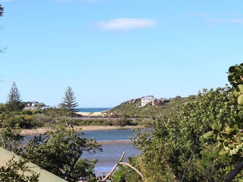 A scenic view overlooking a coastal landscape with a lagoon, surrounding vegetation, and distant residential properties near the ocean.