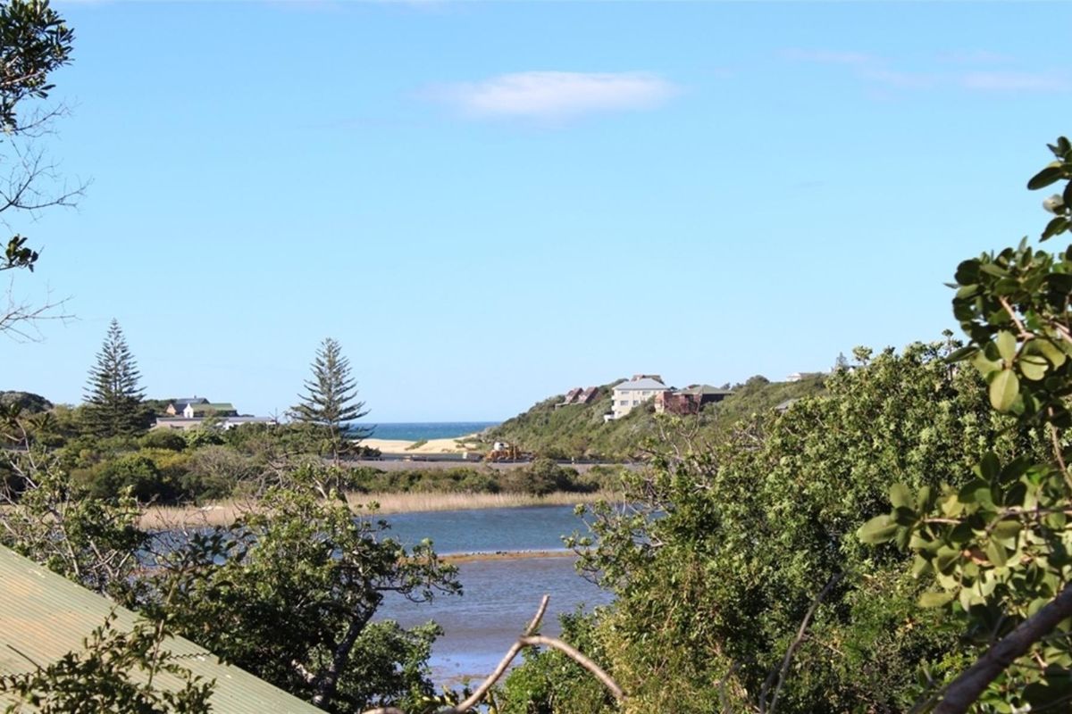 A scenic view overlooking a coastal landscape with a lagoon, surrounding vegetation, and distant residential properties near the ocean.