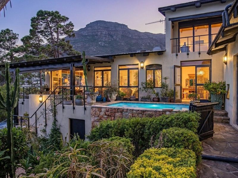 Rear elevation featuring a swimming pool, stone-clad retaining wall, covered patio, and balcony with mountain views.