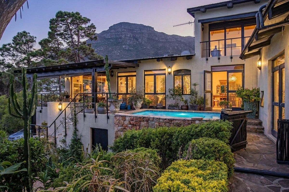 Rear elevation featuring a swimming pool, stone-clad retaining wall, covered patio, and balcony with mountain views.