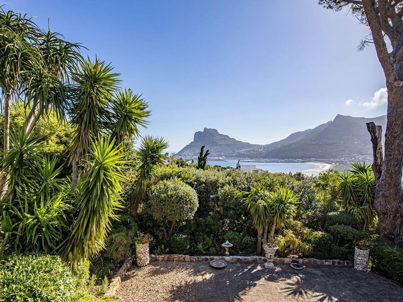 A scenic outdoor view featuring a landscaped garden, stone patio, and expansive coastal mountain vistas.