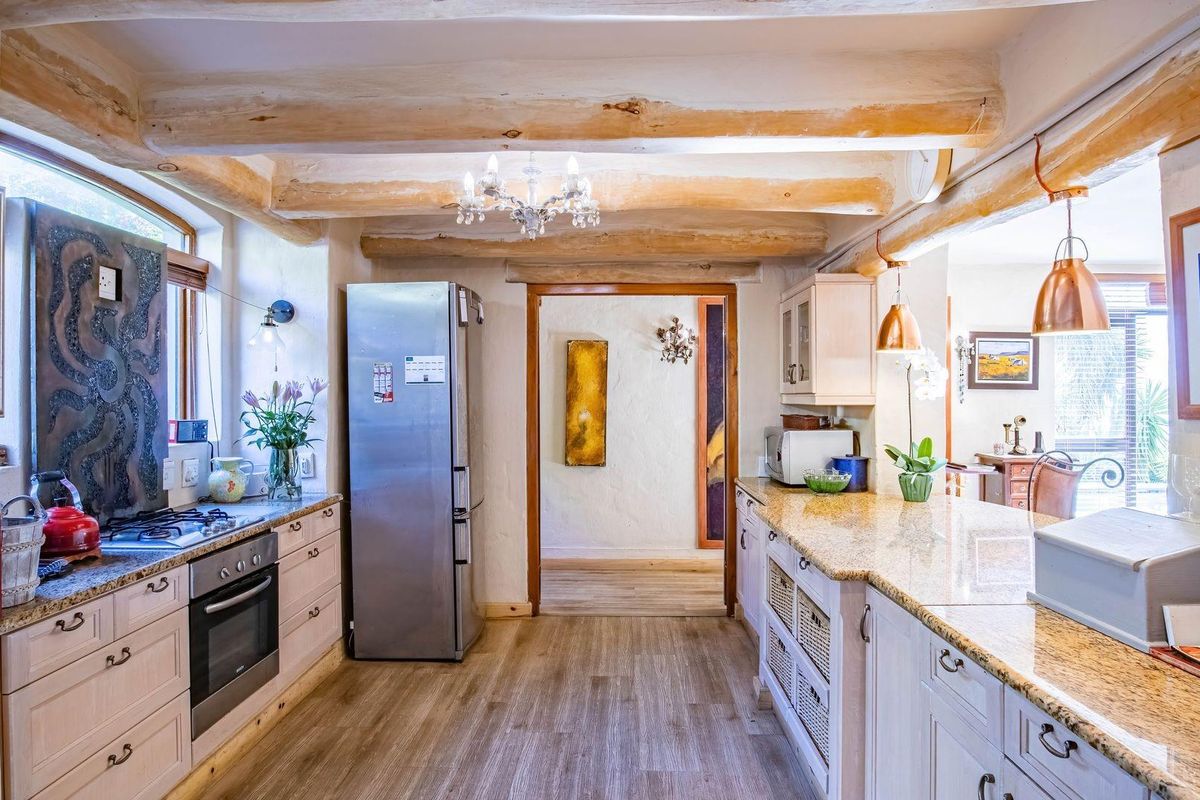 A charming kitchen featuring exposed timber ceiling beams, granite countertops, fitted cabinetry, and a built-in oven with a gas hob.