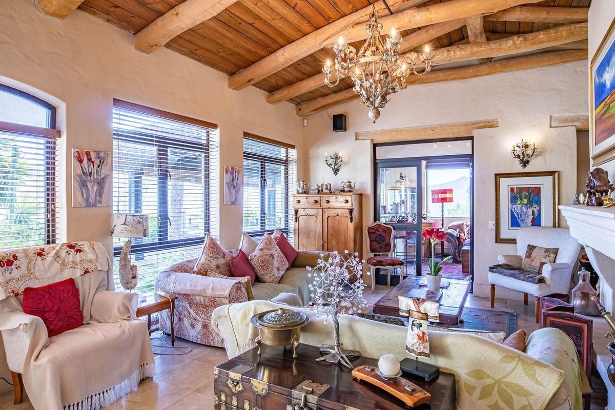 Spacious living room featuring a rustic exposed timber beam ceiling, stone fireplace, and large windows that provide ample natural light.