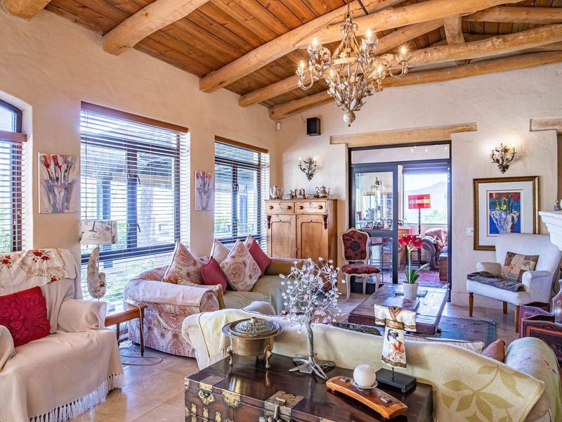 Spacious living room featuring a rustic exposed timber beam ceiling, stone fireplace, and large windows that provide ample natural light.