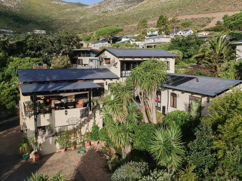Aerial view of a multi-level residential property featuring a corrugated metal roof, solar panels, and a spacious covered patio set within a landscaped garden.
