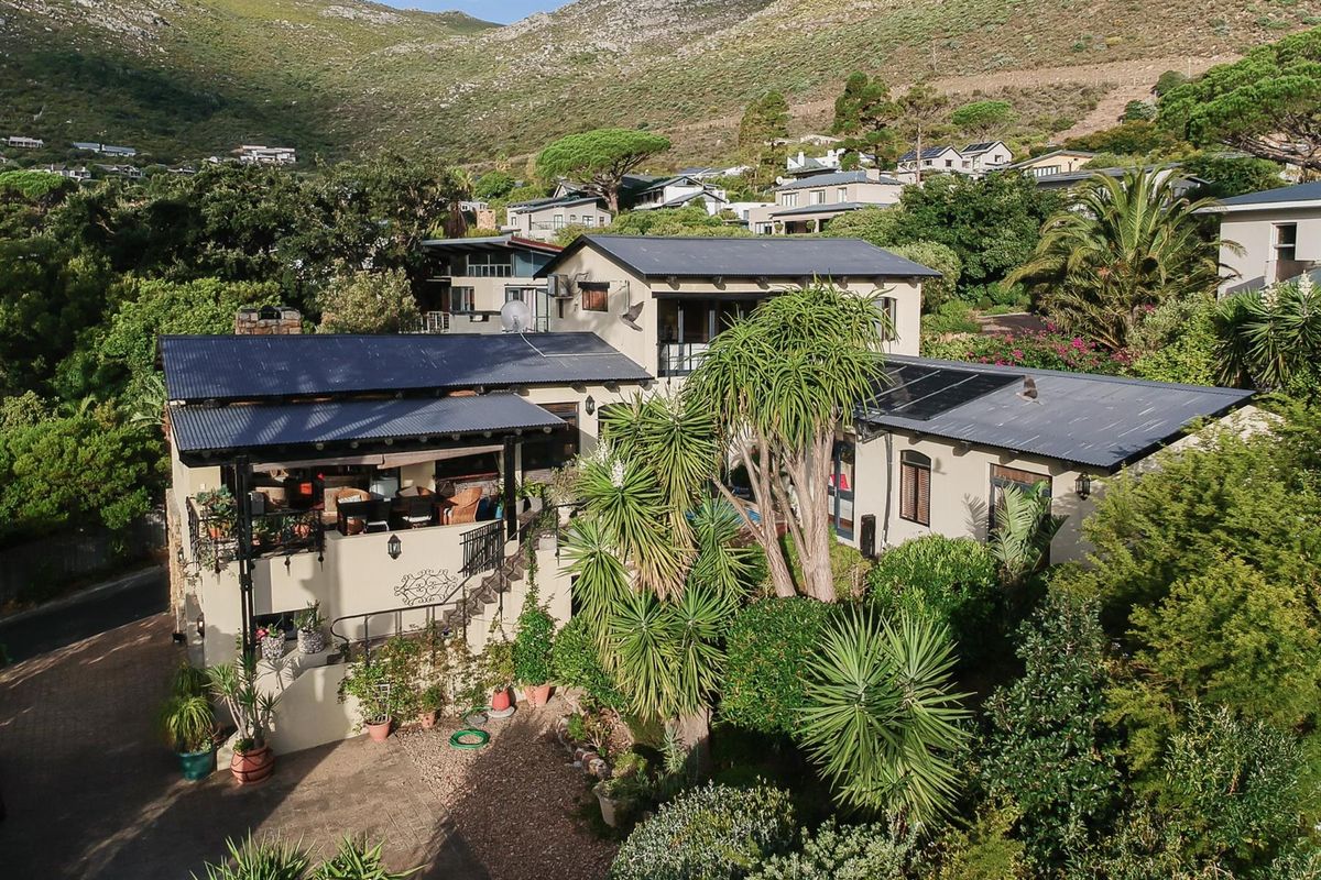Aerial view of a multi-level residential property featuring a corrugated metal roof, solar panels, and a spacious covered patio set within a landscaped garden.
