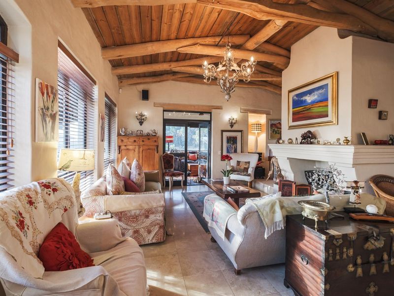 Spacious living room featuring a rustic exposed timber beam ceiling, a prominent stone fireplace, and large windows with venetian blinds leading to the patio.
