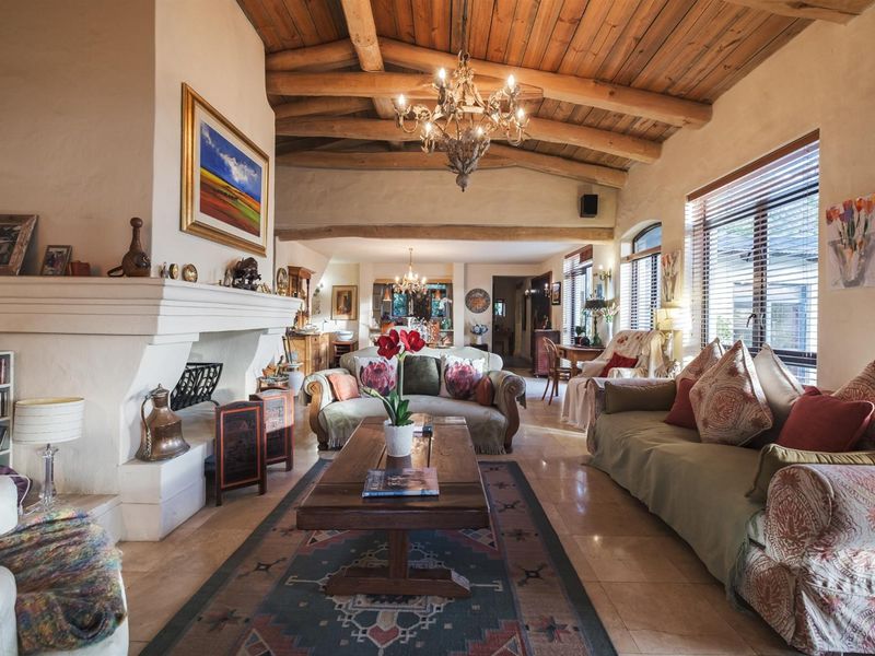 Spacious living room featuring a high exposed timber beam ceiling, stone fireplace, and large windows with venetian blinds, creating a warm and inviting atmosphere.