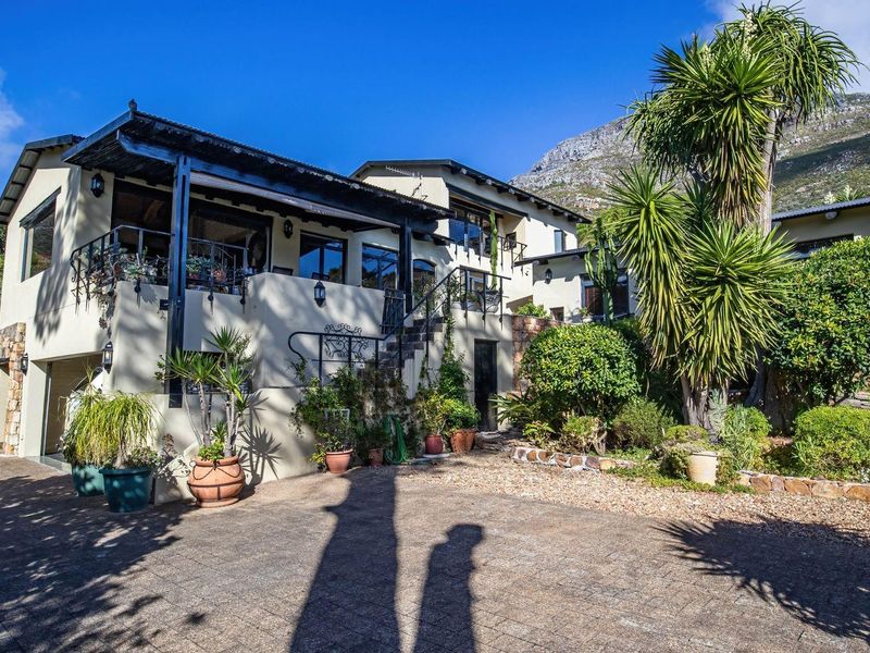 A multi-level residential property featuring a paved driveway, covered balcony with wrought iron railings, and stone accents set against a mountain backdrop.