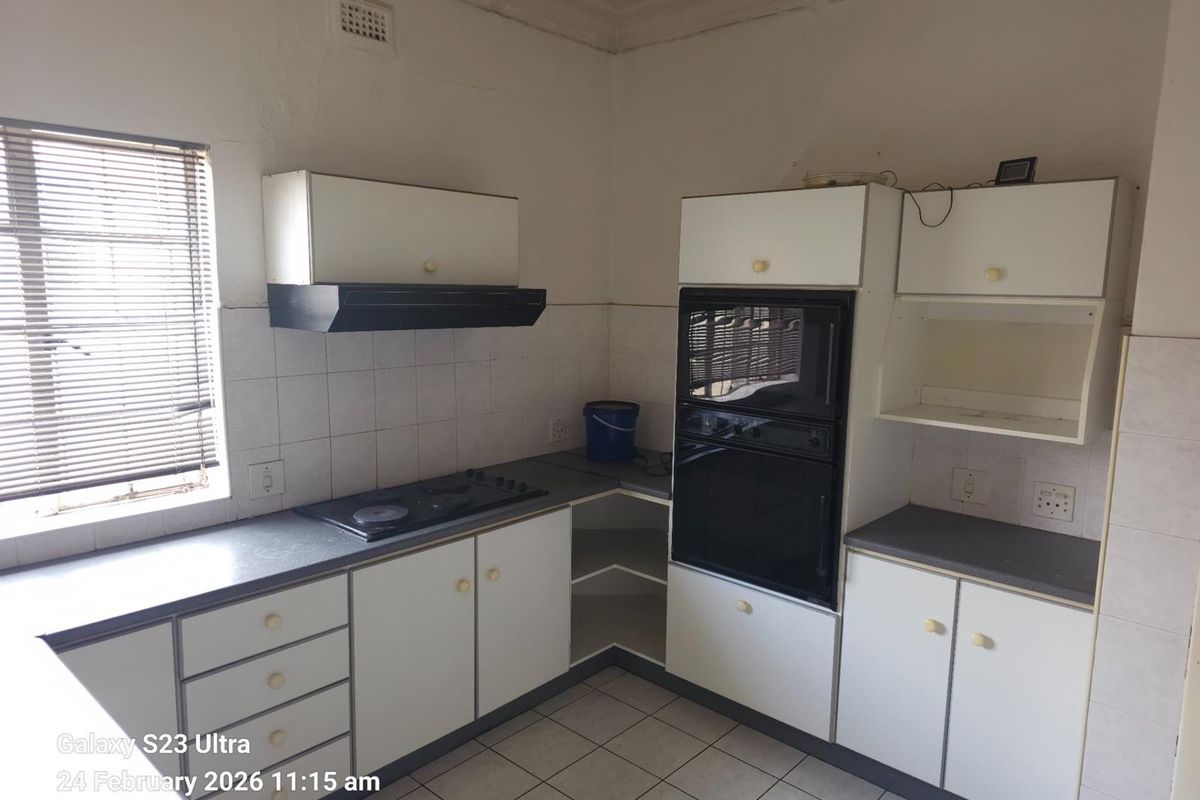 A dated kitchen featuring white cabinetry, built-in oven, hob, extractor fan, and tiled flooring, offering a functional layout in need of modernization.