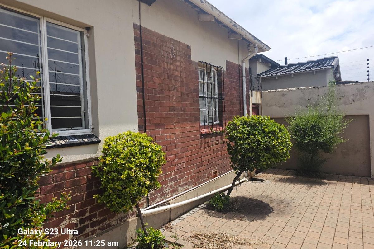 Exterior view of the side of the house featuring a brick and plaster facade, security bars on windows, and paved ground area.
