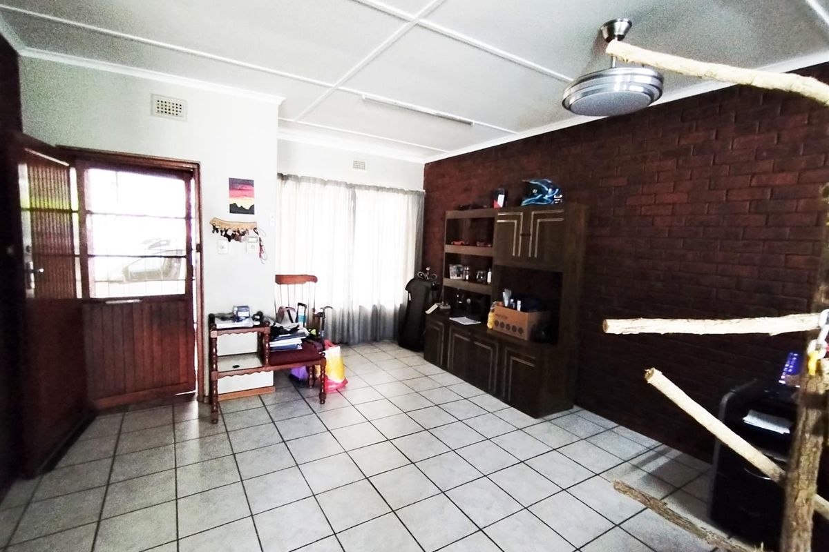 Living room featuring tiled flooring, an exposed brick feature wall, and a ceiling fan, providing a functional space with potential for modernization.